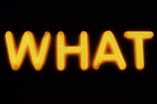 Bright yellow neon 'What' sign glowing against a black background in Budapest, Hungary.